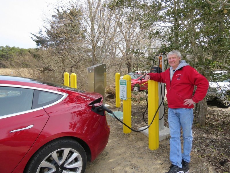 Man smiling and leaning against an electric car charging station while his car charges.